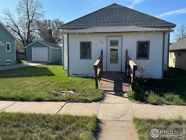 109 E 5th St, Julesburg, CO 80737 - bungalow-style house with an outbuilding, a garage, stucco siding, roof with shingles, and a front lawn