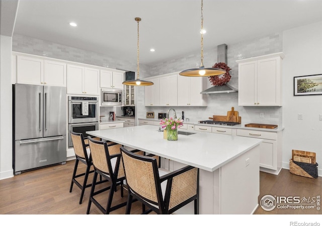 kitchen featuring appliances with stainless steel finishes, wall chimney exhaust hood, a sink, dark wood-type flooring, and white cabinetry