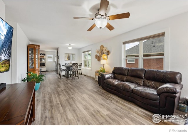 living room with light wood-style flooring, baseboards, and a ceiling fan