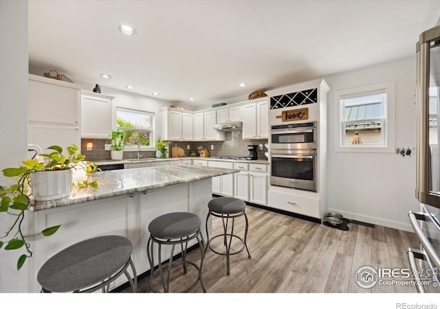 kitchen featuring a breakfast bar area, white cabinetry, under cabinet range hood, appliances with stainless steel finishes, and decorative backsplash