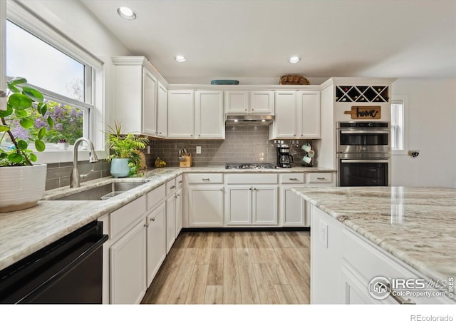 kitchen with a sink, stainless steel appliances, light wood-style flooring, decorative backsplash, and white cabinets