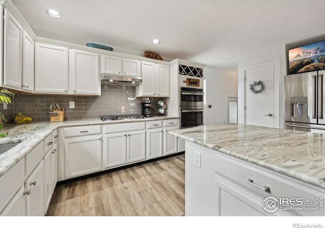 kitchen featuring stainless steel appliances, white cabinets, light wood-type flooring, backsplash, and under cabinet range hood