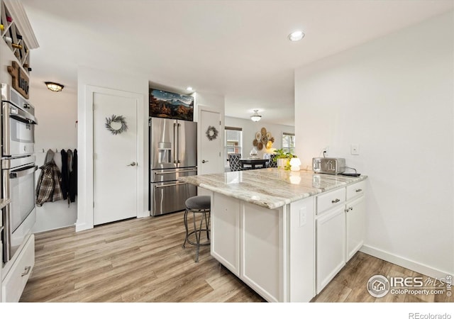 kitchen with light stone counters, a peninsula, light wood-style floors, white cabinets, and appliances with stainless steel finishes