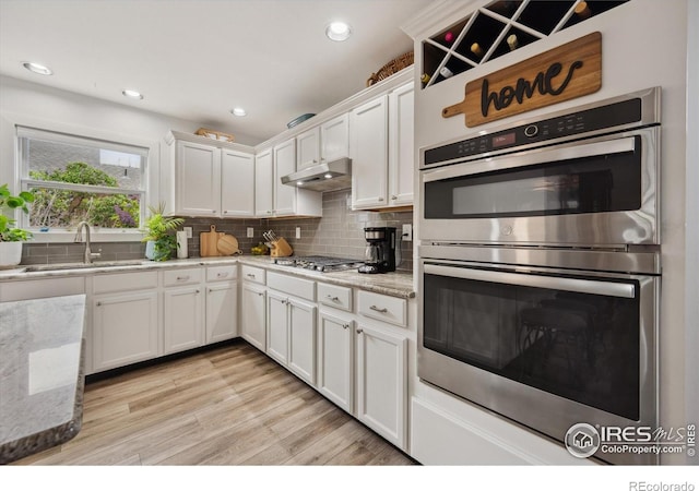 kitchen with under cabinet range hood, tasteful backsplash, a sink, white cabinets, and appliances with stainless steel finishes