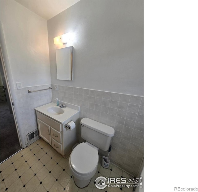 half bathroom with tile walls, toilet, wainscoting, visible vents, and vanity