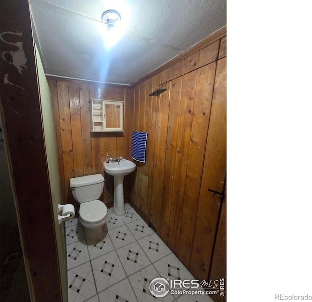 half bath with tile patterned floors, toilet, and wooden walls
