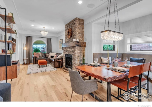 dining area with crown molding, wood-type flooring, a notable chandelier, and a stone fireplace