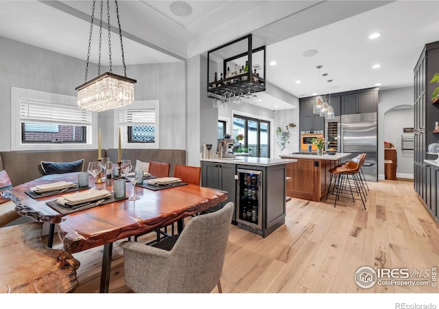 dining room with wine cooler, arched walkways, light wood-type flooring, and an inviting chandelier