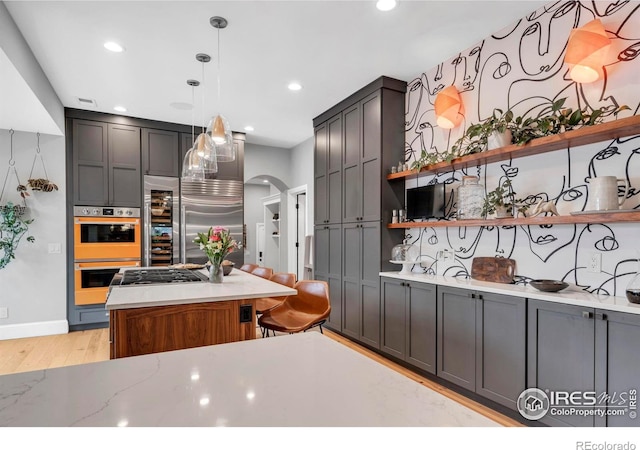 kitchen with open shelves, light wood-style floors, arched walkways, appliances with stainless steel finishes, and recessed lighting