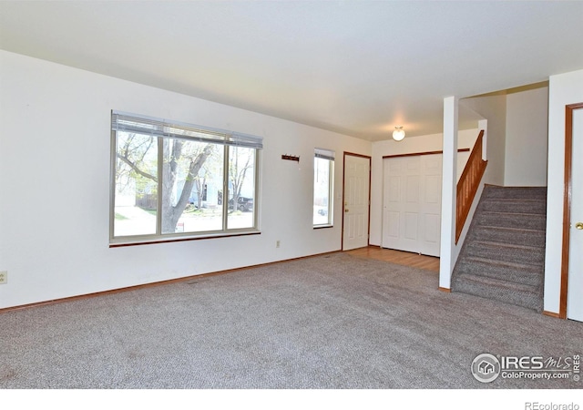 unfurnished living room with baseboards, stairway, and carpet