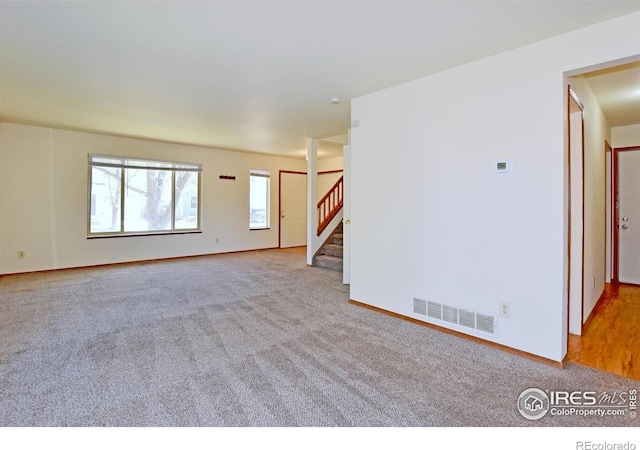 carpeted spare room featuring visible vents, baseboards, and stairs