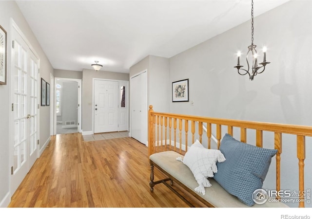 foyer entrance with light wood finished floors, an inviting chandelier, visible vents, and baseboards