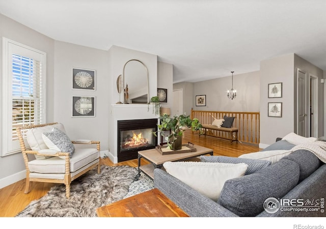 living room featuring baseboards, a notable chandelier, a glass covered fireplace, and wood finished floors