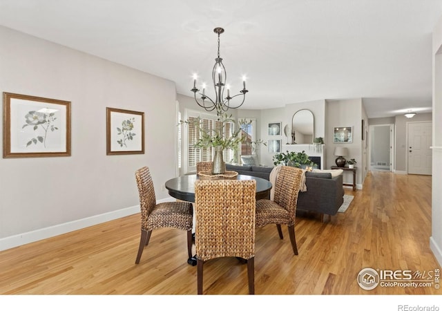 dining room with a warm lit fireplace, a notable chandelier, baseboards, and light wood-style floors