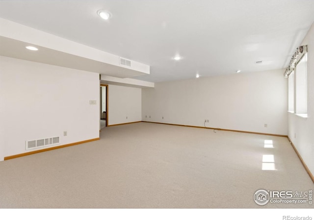 basement featuring baseboards, visible vents, and light colored carpet