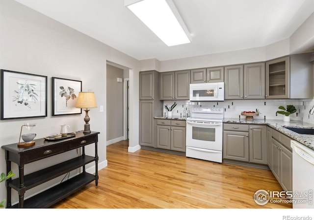 kitchen with glass insert cabinets, a sink, gray cabinets, white appliances, and decorative backsplash