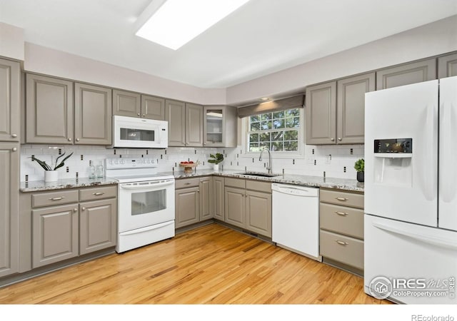 kitchen with gray cabinetry, tasteful backsplash, a sink, and white appliances