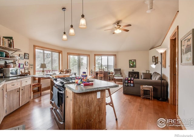 kitchen featuring light wood finished floors, ceiling fan, gas range, open shelves, and a kitchen island