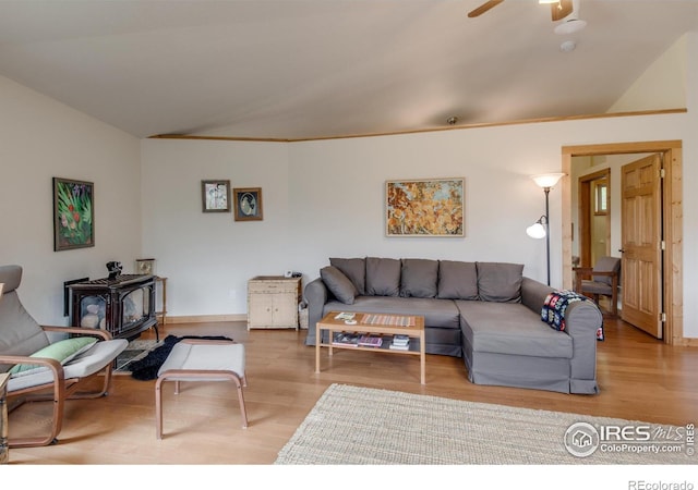living room with wood finished floors, a wood stove, vaulted ceiling, ceiling fan, and baseboards