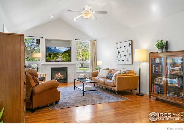 112 Cobble Dr, Windsor, CO 80550 - living area featuring lofted ceiling, a glass covered fireplace, a ceiling fan, and wood finished floors