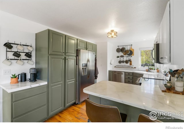 112 Cobble Dr, Windsor, CO 80550 - kitchen with a peninsula, light wood finished floors, a kitchen bar, green cabinets, and appliances with stainless steel finishes