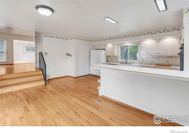 kitchen with freestanding refrigerator, light wood finished floors, a sink, decorative backsplash, and light countertops