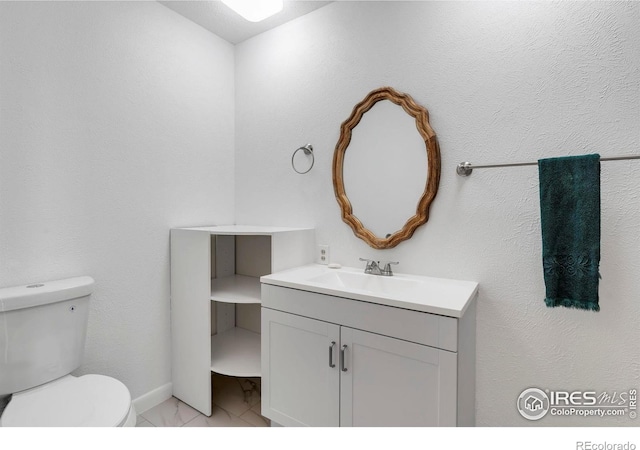 half bathroom with toilet, baseboards, marble finish floor, and vanity