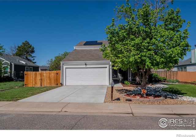 view of property hidden behind natural elements featuring fence, a garage, solar panels, concrete driveway, and a front lawn