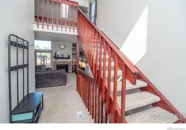 stairs with carpet flooring, a tile fireplace, and a high ceiling