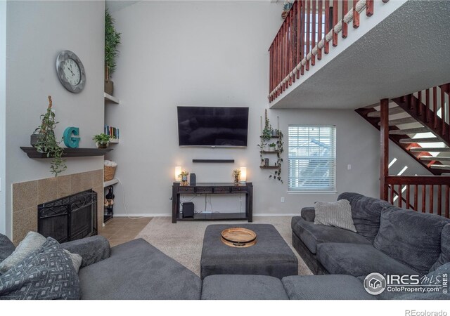 tiled living area featuring a fireplace, stairs, a high ceiling, and baseboards