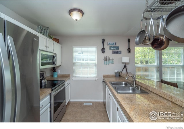 kitchen featuring a sink, tile patterned flooring, white cabinetry, baseboards, and appliances with stainless steel finishes