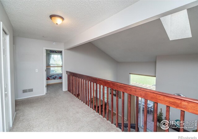 hall featuring baseboards, a textured ceiling, visible vents, and carpet floors