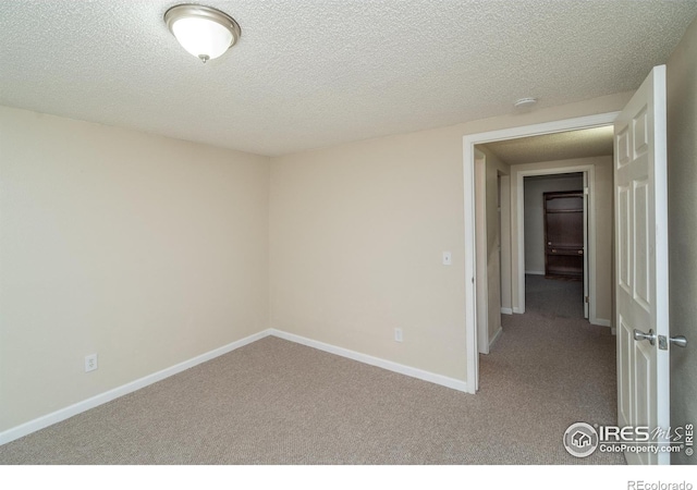 carpeted spare room featuring a textured ceiling and baseboards