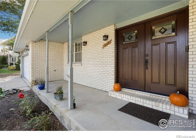 entrance to property with a porch, brick siding, and an attached garage