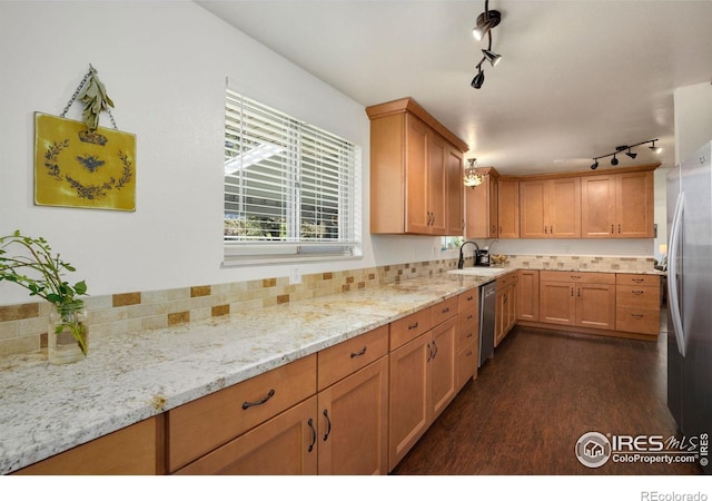 kitchen featuring light stone counters, dark wood finished floors, a sink, track lighting, and stainless steel appliances