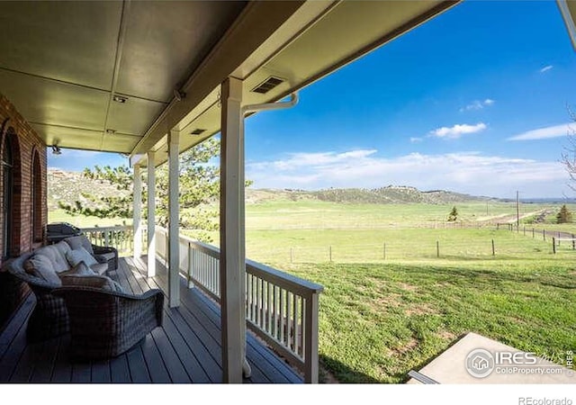 deck with covered porch, a rural view, fence, and a lawn