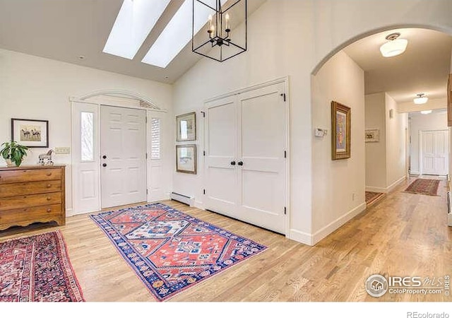 foyer with high vaulted ceiling, baseboards, arched walkways, light wood-style floors, and a baseboard radiator