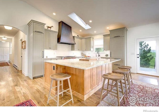 kitchen with vaulted ceiling with skylight, a breakfast bar area, gray cabinets, and custom range hood