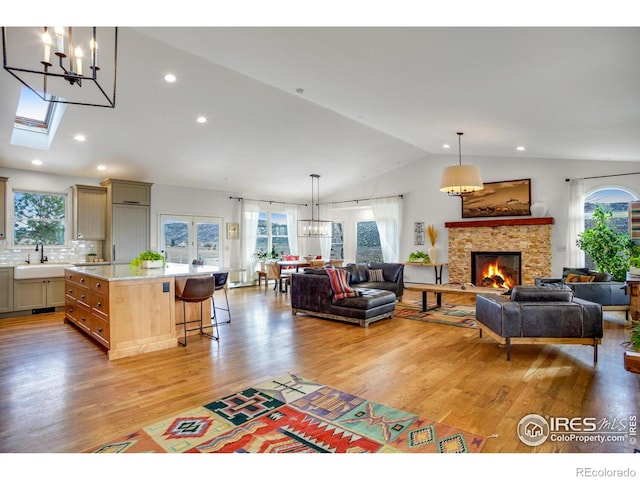 living room featuring lofted ceiling, a chandelier, healthy amount of natural light, a stone fireplace, and light wood-style floors