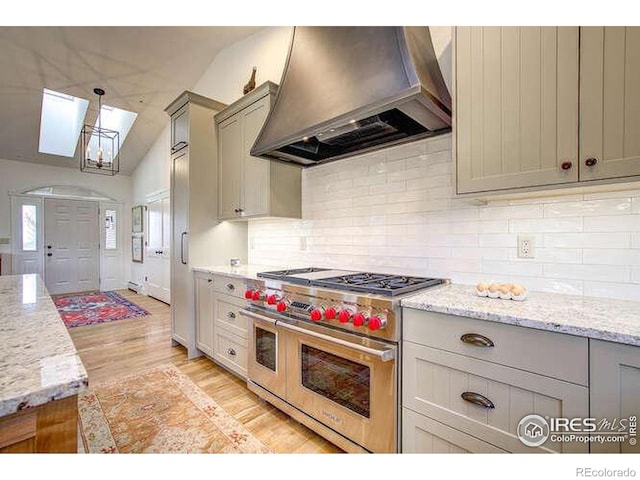 kitchen with custom exhaust hood, double oven range, gray cabinetry, vaulted ceiling, and light wood finished floors