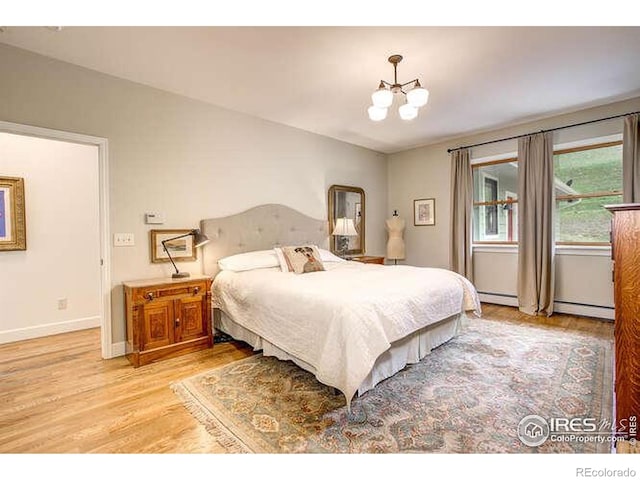 bedroom featuring a chandelier, light wood-style floors, a baseboard radiator, and baseboards