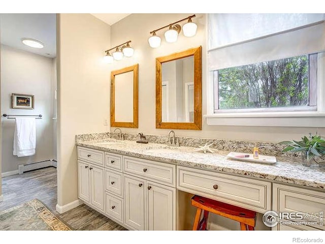 bathroom featuring baseboard heating, double vanity, wood finished floors, and baseboards