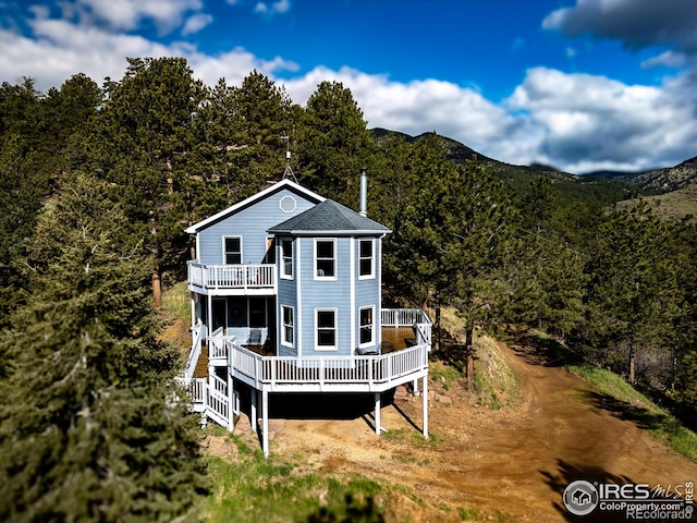back of property featuring a balcony, a forest view, and a deck