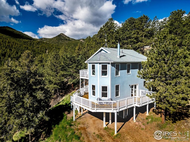 back of property with a balcony, a wooded view, a wooden deck, and roof with shingles