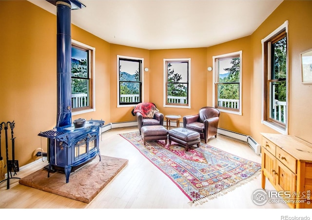 sitting room with a wood stove, healthy amount of natural light, a baseboard radiator, and wood finished floors