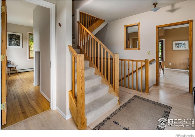stairway featuring hardwood / wood-style floors, baseboard heating, and baseboards