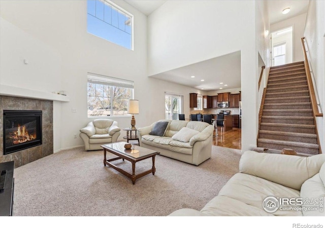 carpeted living area featuring a towering ceiling, stairs, and a tile fireplace