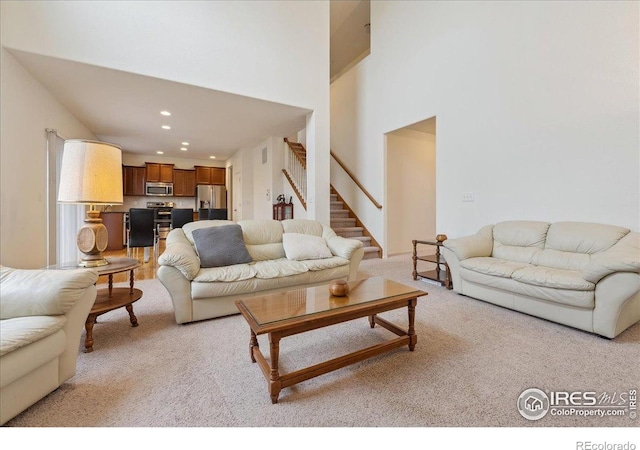 living area featuring light colored carpet, stairway, recessed lighting, and a towering ceiling