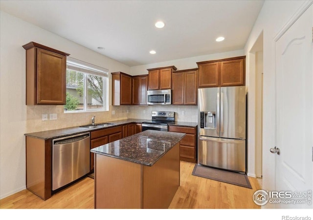kitchen featuring stainless steel appliances, a sink, light wood-style flooring, dark stone countertops, and tasteful backsplash