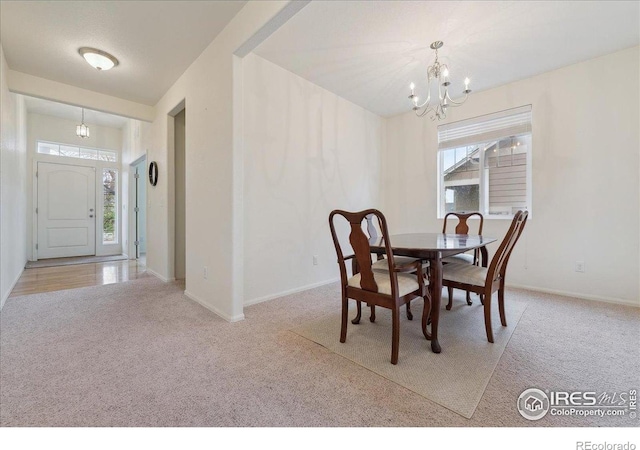 carpeted dining area with a chandelier and baseboards